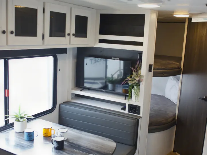 This RV rental interior showcases a cozy dinette, TV entertainment, and bunk beds, ideal for family travel adventures.. Heartland Trail Runner 2022