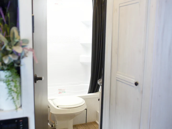 Compact RV rental bathroom with white toilet, shower/tub, black curtain, and light wooden details.. Heartland Trail Runner 2022