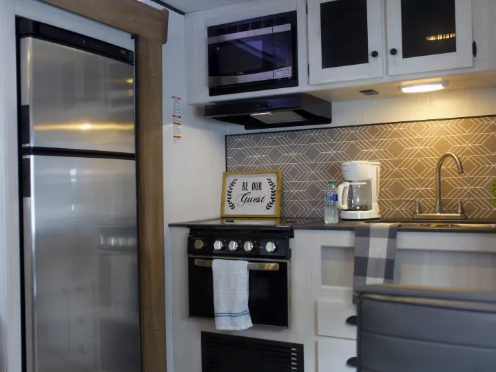 Modern rv rental kitchen with stainless steel fridge, microwave, stove, sink, and stylish patterned backsplash.. Heartland Trail Runner 2022