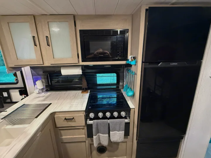 Compact RV rental kitchen featuring modern Furrion appliances: fridge, microwave, stove, sink, and light wood cabinets.. Forest River Wildwood X-Lite Platinum 2024