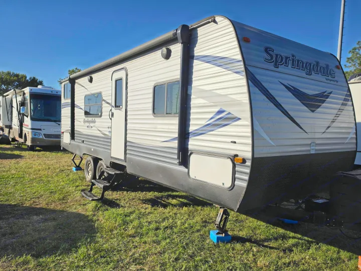 A Springdale travel trailer, potentially an RV rental, is parked on grass with a motorhome behind it on a clear day.. Keystone RV Springdale SSR 2018
