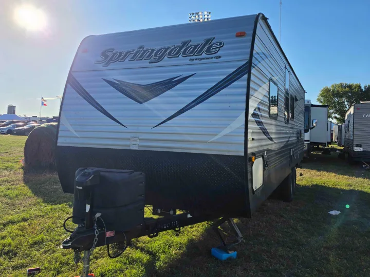 This Springdale by Keystone travel trailer RV rental is parked on green grass under a clear, bright sky, ready for a trip.. Keystone RV Springdale SSR 2018