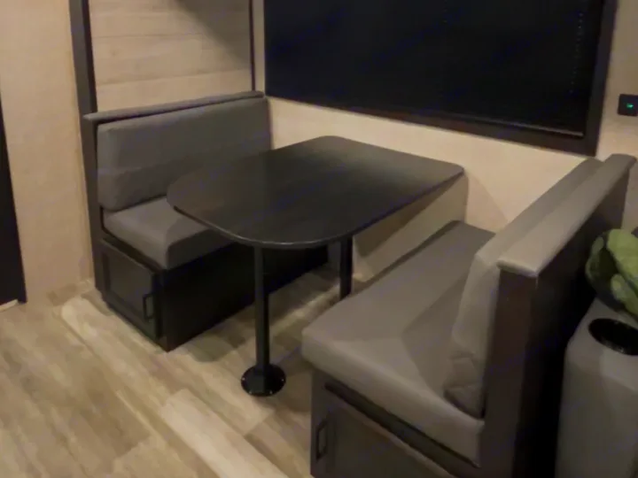 This RV rental dinette features gray booth seating and a dark table. A cozy interior setup with wood-look flooring and a window.. Jayco Jay Flight 2023