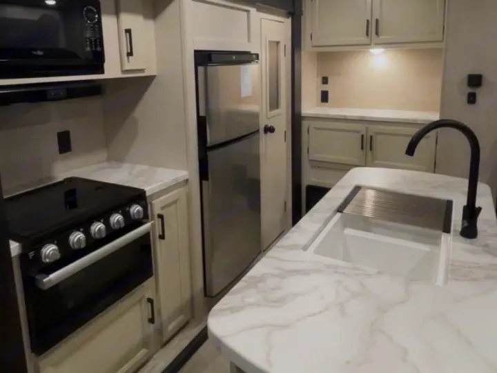 Modern RV rental kitchen: microwave, stove, refrigerator, and island sink with a drying rack on marble-look counters.. Jayco Jay Flight 2023