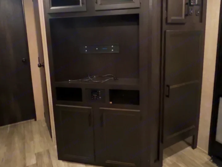 RV rental living space: A dark wood entertainment unit with TV mount, storage cabinets, & a media player provides interior functionality.. Jayco Jay Flight 2023
