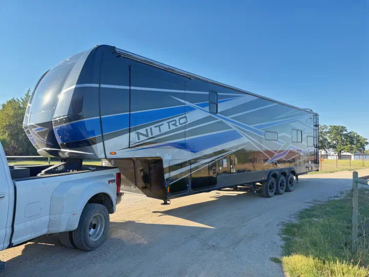 This Nitro fifth-wheel toy hauler RV rental is hitched to a dually truck, parked on a gravel drive, ready for travel.. Forest River XLR Nitro Toy Hauler 2023