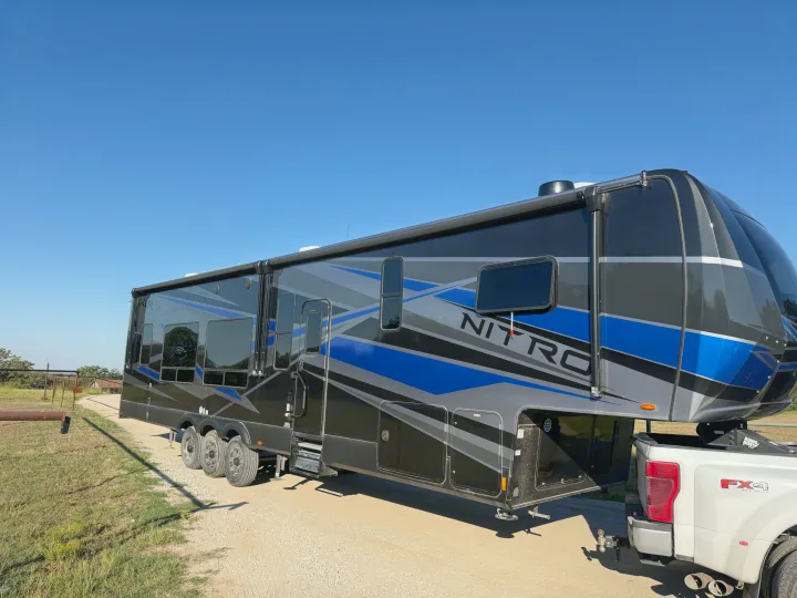 This large black, blue, and gray Nitro fifth-wheel RV rental is ready for adventure, hitched to a white FX4 pickup truck.. Forest River XLR Nitro Toy Hauler 2023