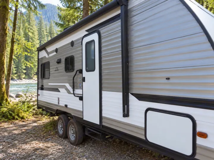RV rental: A travel trailer is parked by a scenic river in a lush forest, ready for outdoor adventures.. Aspen Trail 2180RDWE 2020