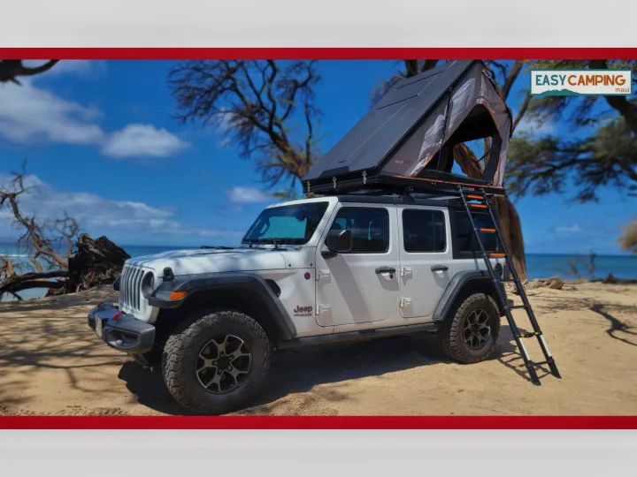 A white Jeep Wrangler with a deployed rooftop tent and ladder, parked on a beach, ready for your RV rental camping trip.. Jeep Wrangler 2025
