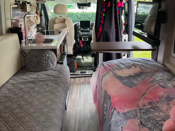 Cozy RV rental interior: view of two beds, a compact kitchen, table, and driver's area, ideal for road trips.. Winnebago Travato 2024