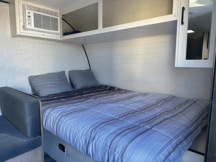 Experience comfort in this RV rental bedroom: striped bed, cozy pillows, integrated AC, and overhead storage.. Jayco Jay Flight 2025