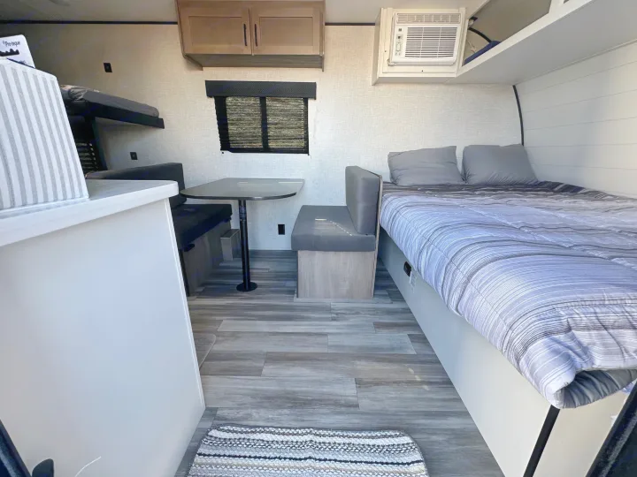 Interior view of a modern RV rental, featuring bunk beds, a dinette, a comfortable main bed, and an AC unit for a cozy travel experience.. Jayco Jay Flight 2025
