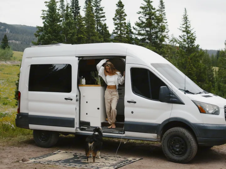 Woman and dog in a scenic mountain setting, stepping out of their RV rental camper van for an adventure.. Ford Transit 2015