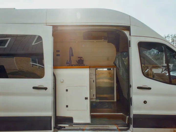 Inside this modern **rv rental**, a converted van reveals a compact kitchen with sink, stove, and mini-fridge for travel.. Ford Transit 2015