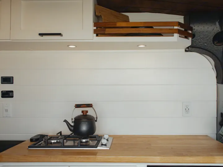 RV rental van conversion kitchen: gas stove, kettle, wooden counter, white shiplap, and practical storage.. Ford Transit 2015