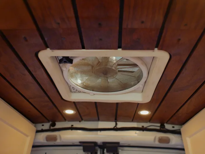 Overhead view of a cozy rv rental van ceiling with warm wood planks, a central ventilation fan, and recessed LED lighting.. Ford Transit 2015