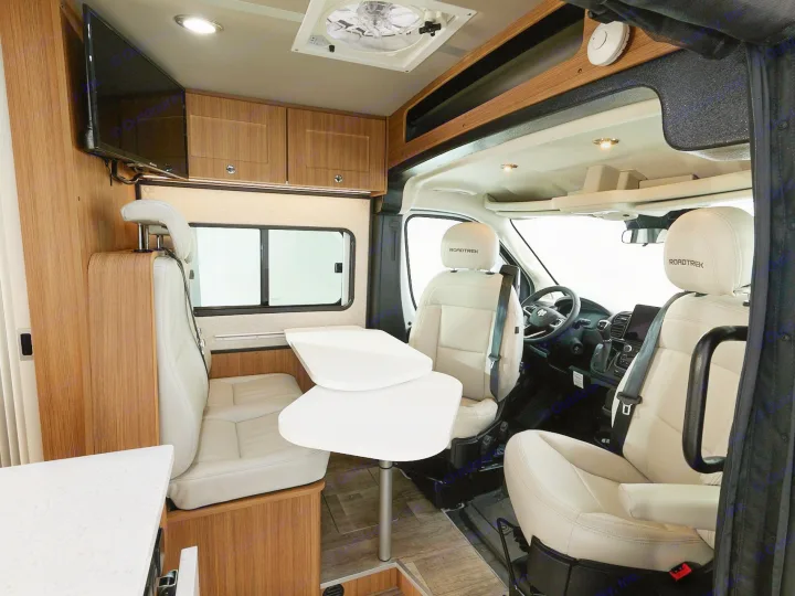 Spacious RV rental interior with a light-colored dining area, swiveling front seats, TV, and wood-paneled storage.. Roadtrek PIVOT SLUMBER 2024
