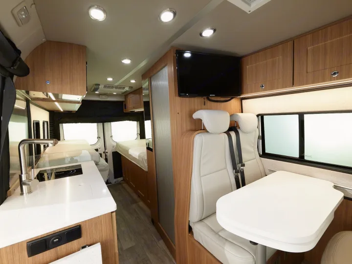 RV rental interior: modern kitchenette, dining table with TV, and rear sleeping area. Perfect for comfortable travel.. Roadtrek PIVOT SLUMBER 2024