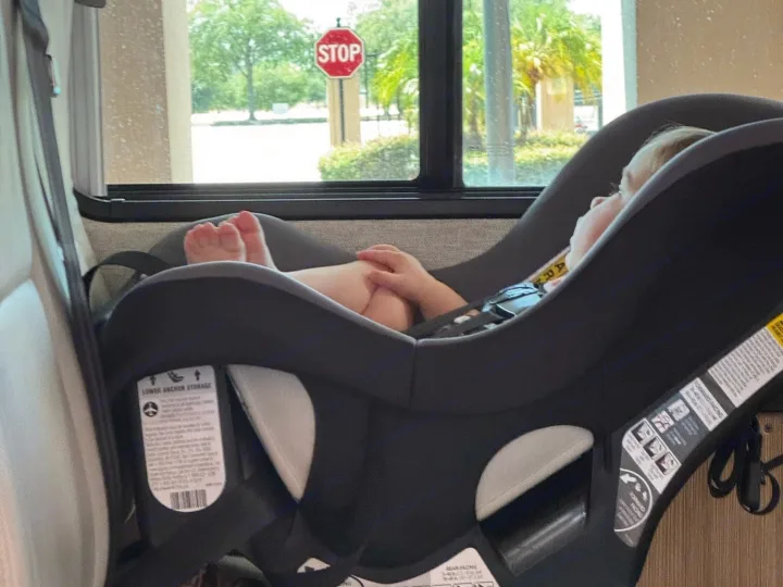 Safe and sound! A baby rests in a car seat inside an RV rental, with a view of a "STOP" sign outside.. Roadtrek PIVOT SLUMBER 2024