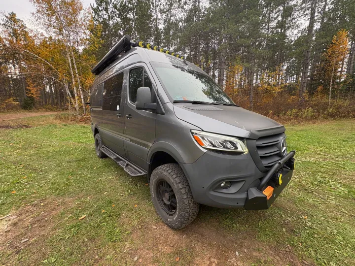 Customized gray Mercedes-Benz Sprinter overland van, ideal for rv rental, surrounded by autumn trees on a dirt path.. Storyteller Overland Storyteller Overland Class B 2024