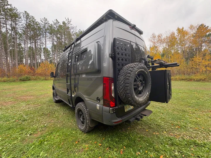 Gray off-road camper van, perfect for your next rv rental adventure, parked in a forest with autumn trees.. Storyteller Overland Storyteller Overland Class B 2024