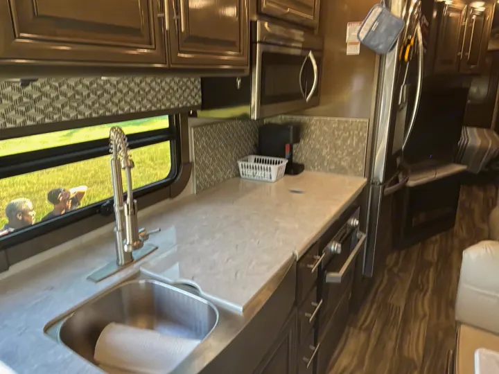Modern RV rental kitchen with sink, microwave, and cabinets. Two people are visible outside the window.. Georgetown GT7 2022