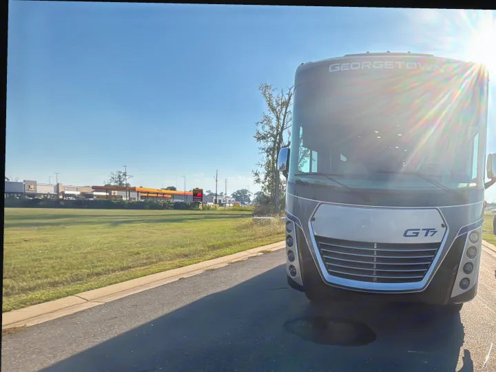 A large, modern Georgetown GT7 RV, possibly an RV rental, faces forward on a sunny day with lens flare. Gas station visible behind.. Georgetown GT7 2022