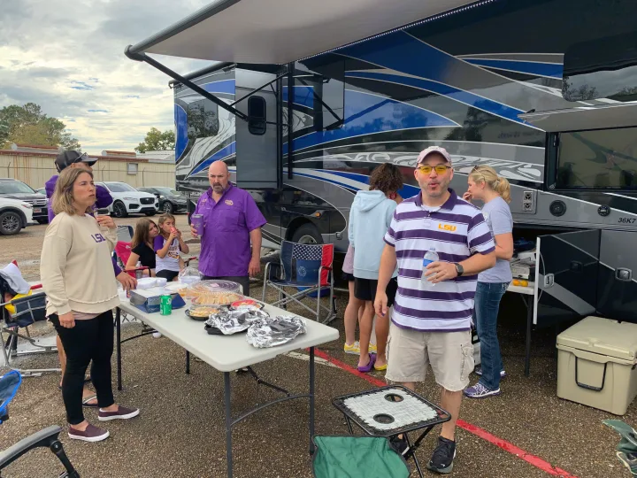 Friends enjoy a tailgate party with food next to an RV rental, showing LSU spirit under its awning.. Georgetown GT7 2022