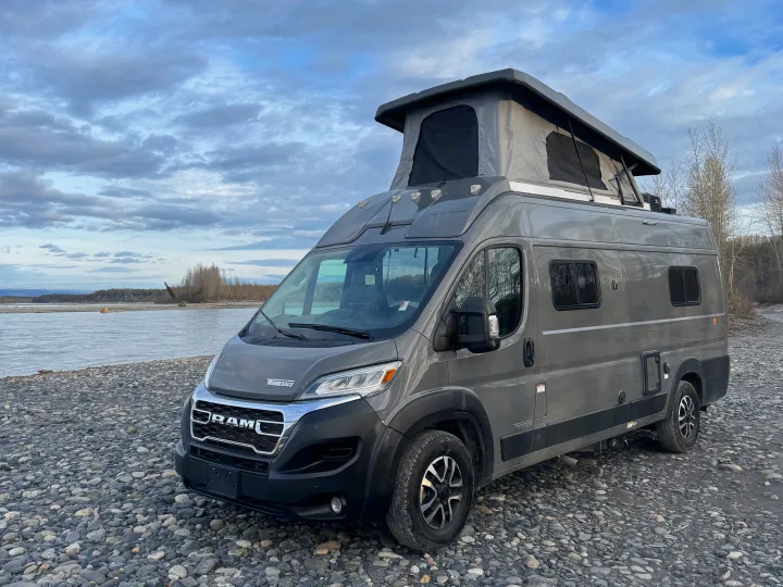 This gray Winnebago Solis rv rental, a pop-top camper van, is parked on a rocky riverbank for outdoor adventure.. Winnebago Solis 59PX 2025