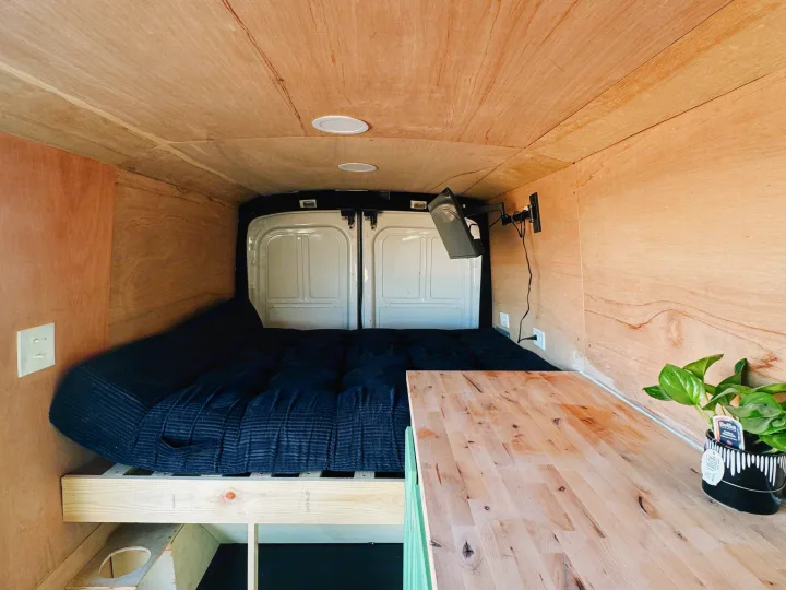 Cozy camper van interior with a bed, wooden panels, TV, and plant. Ready for your next RV rental road trip adventure!. Ford Transit 2016