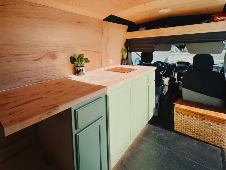 Modern campervan kitchen in an RV rental, featuring light wood paneling, mint cabinets, and wooden countertops for mobile living.. Ford Transit 2016