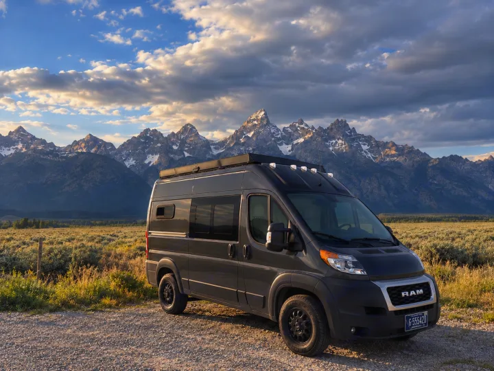 Explore with an RV rental! A gray camper van sits before majestic, snow-capped mountains and a vast plain.. Dodge Ram 1500 2020
