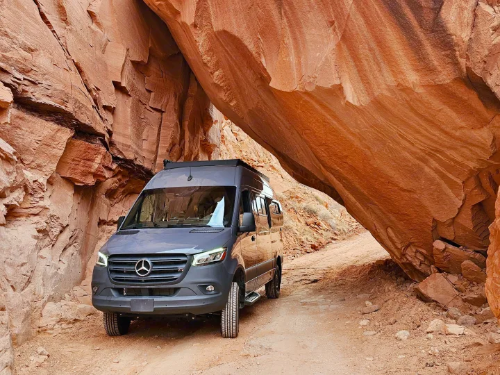 An RV rental Sprinter van navigates a dramatic red rock canyon. This camper van adventure is perfect for off-road exploration.. Mercedes-Benz Sprinter 2023