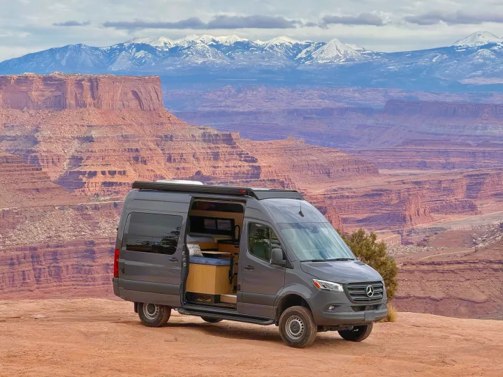 An RV rental Sprinter camper van enjoys epic road trip views of red rock canyons and distant snow-capped mountains.. Mercedes-Benz Sprinter 2023
