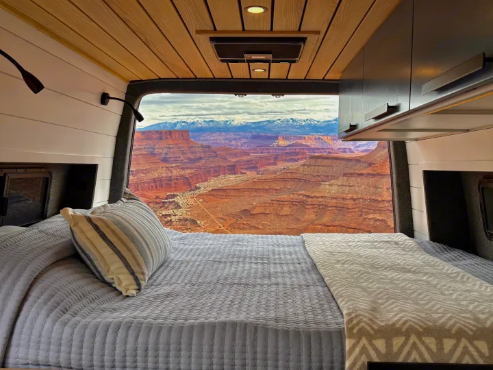 Cozy rv rental bed with a stunning view of red rock canyons and distant snow-capped mountains.. Mercedes-Benz Sprinter 2023