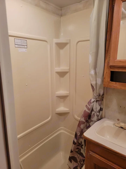 Clean RV rental bathroom featuring a compact shower/tub combo with shelves and a sink vanity, ideal for travel.. Palomino Puma 2005