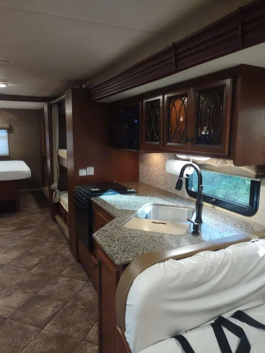RV rental featuring a cozy kitchen with granite-look counter, sink, microwave, stove, dark wood cabinets, and tiled floor.. Thor Windsport 2015