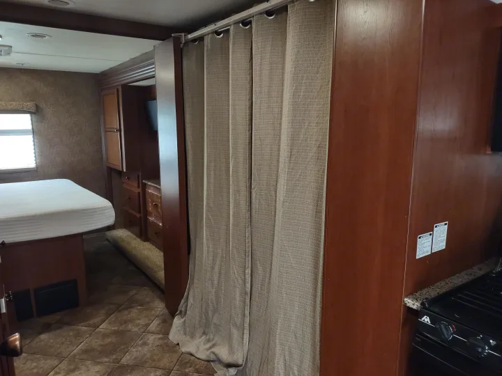 RV rental interior: A cozy bedroom with bed and window, separated by a privacy curtain from the adjacent kitchen area.. Thor Windsport 2015