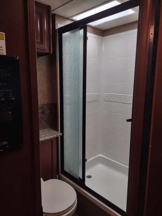 RV rental interior: A compact bathroom featuring a textured glass shower door, white-tiled shower, and toilet.. Thor Windsport 2015