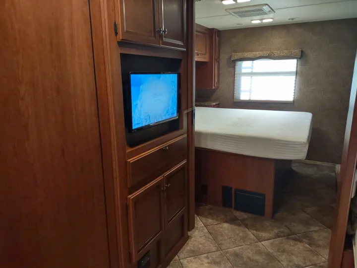 Cozy RV rental bedroom with a large bed, wall-mounted TV, wooden cabinetry, and a window for natural light.. Thor Windsport 2015