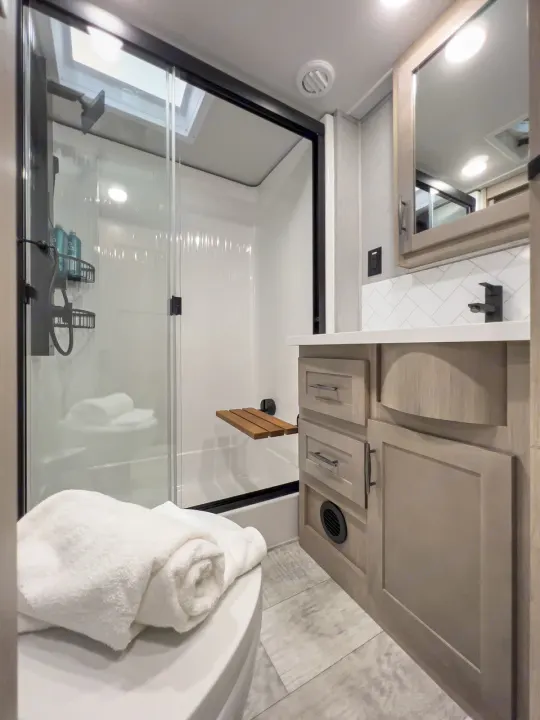 Modern RV rental bathroom: compact with a glass shower, skylight, vanity, and toilet. Bright & functional design.. Grand Design Momentum 2023