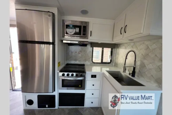 Bright RV rental kitchen with stainless steel fridge, microwave, stove, and sink.. Forest River Palomino Solaire 2023