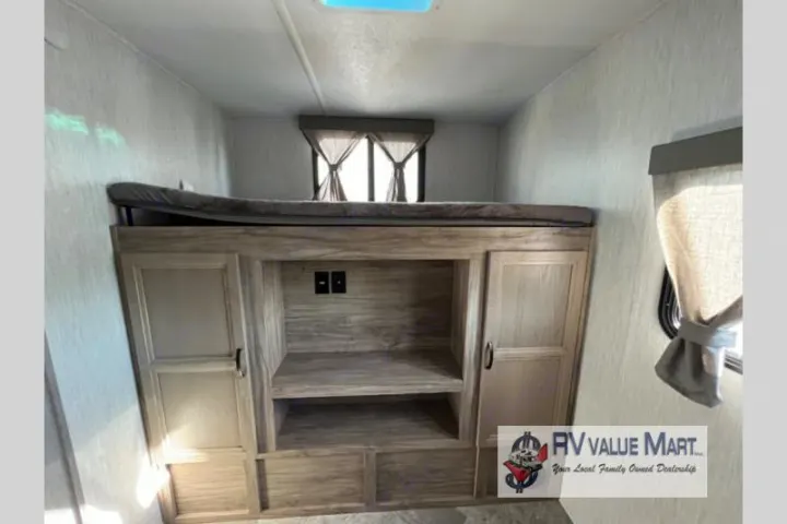 RV rental interior: A cozy bunk bed above wood grain storage cabinets with a media center, ideal for family trips.. Forest River Palomino Solaire 2023