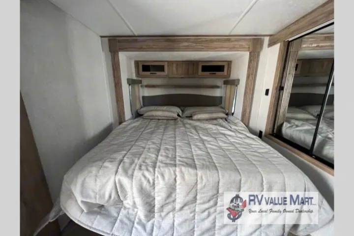 This RV rental bedroom features a comfortable large bed, overhead cabinets for storage, and a mirrored closet for a relaxing stay.. Forest River Palomino Solaire 2023