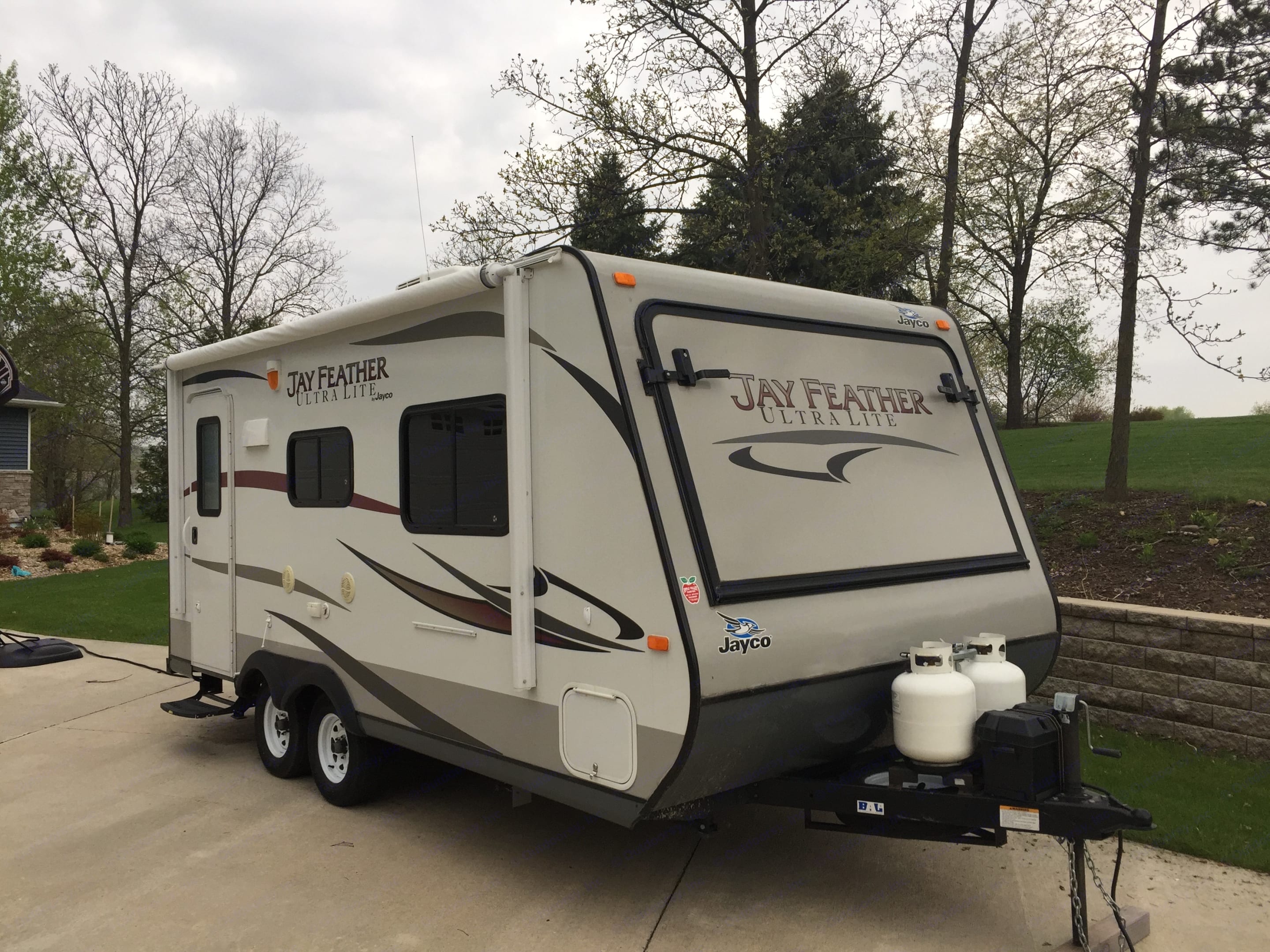 A light grey Jayco Jay Feather Ultra Lite travel trailer, ideal for an rv rental, is parked on a driveway with trees.. Jayco Jay Feather 2013