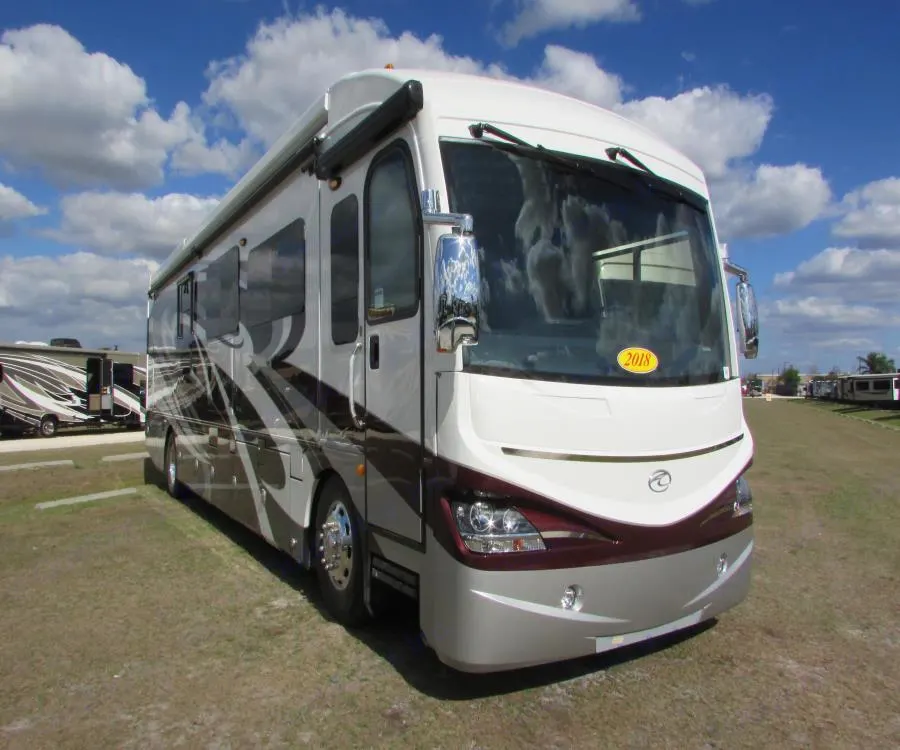 A sleek white, maroon, and silver motorhome (RV), an ideal rv rental, is parked on a grassy lot under blue skies.. American Coach American Dream 2019