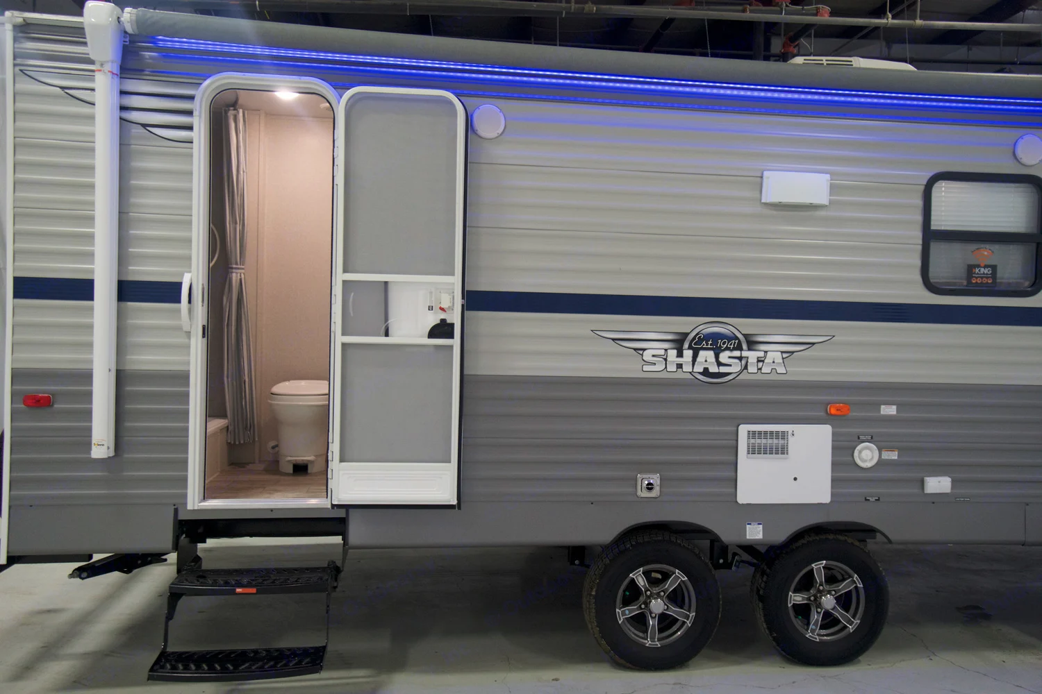 Exterior of a light grey RV rental with blue stripe, main door open to show a compact bathroom. Ideal for camping adventures.. Shasta Shasta 2020