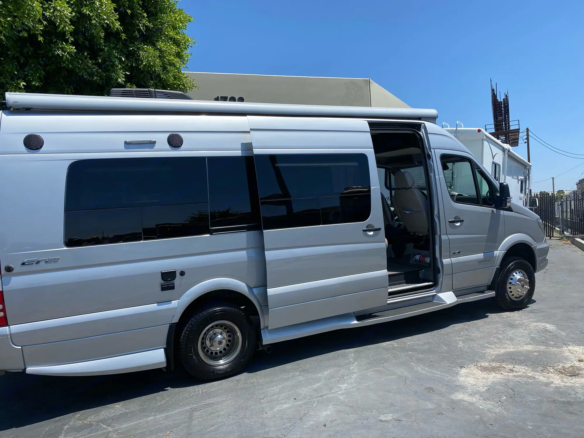 Silver Mercedes Sprinter RV rental: a modern camper van with open side door and extended awning for your travels.. Winnebago Era 4x4 2019