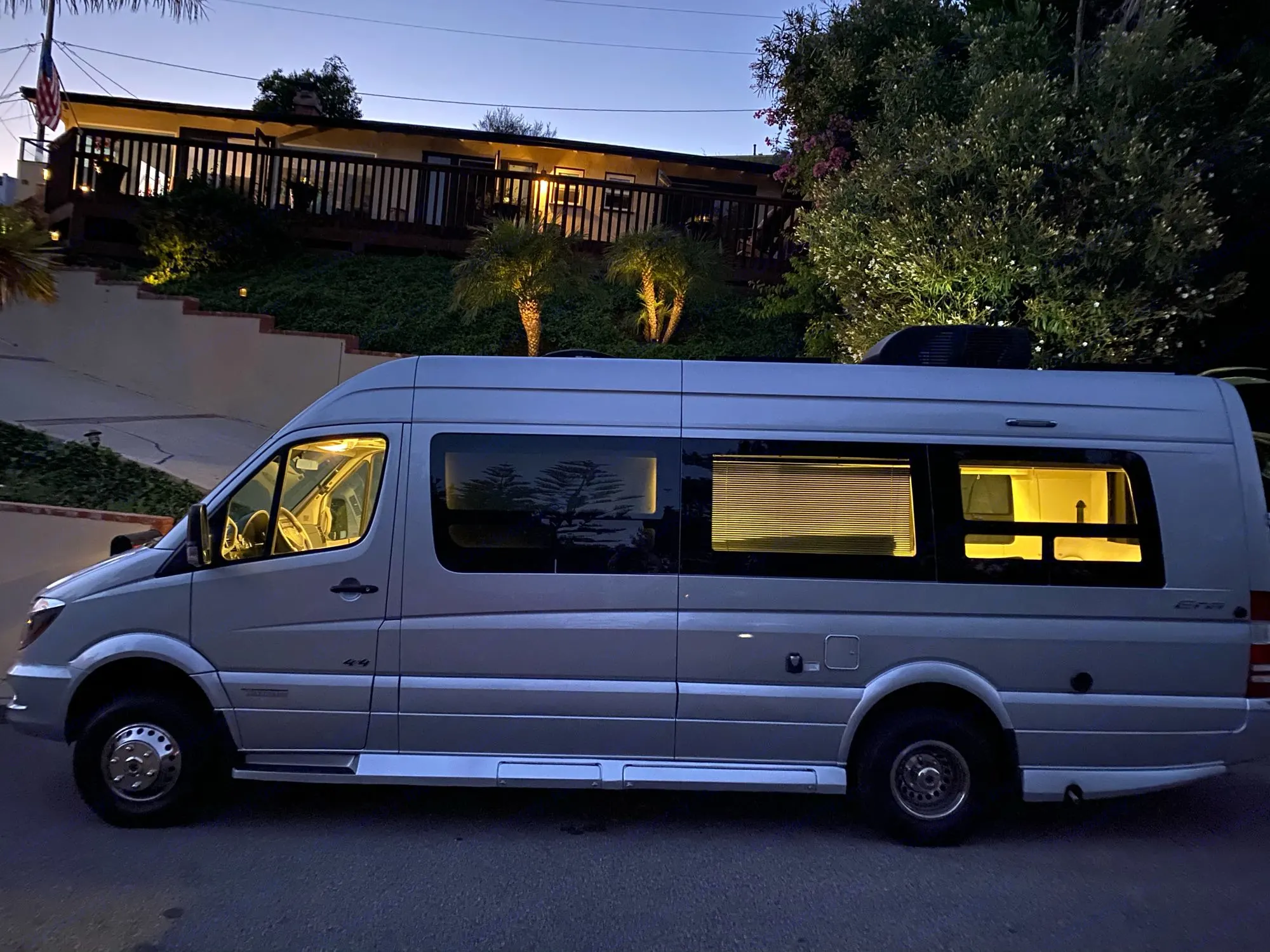 A silver Mercedes-Benz Sprinter RV rental parked at dusk, interior lights on, showcasing its comfortable mobile home setup.. Winnebago Era 4x4 2019