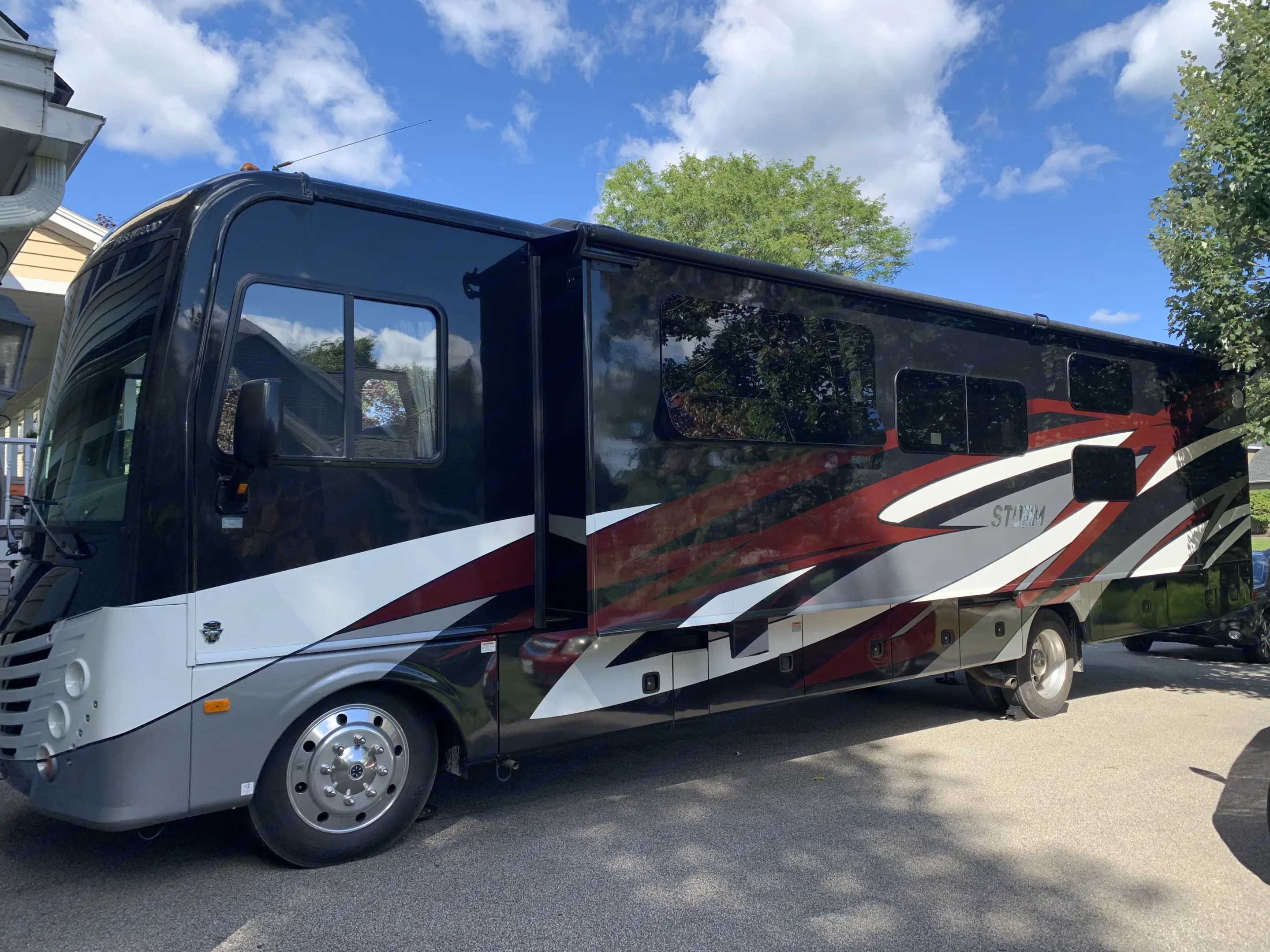 A black, white, and red Fleetwood Storm RV motorhome for rv rental, parked outdoors on a sunny day with extended slide-out.. Fleetwood Storm 2018
